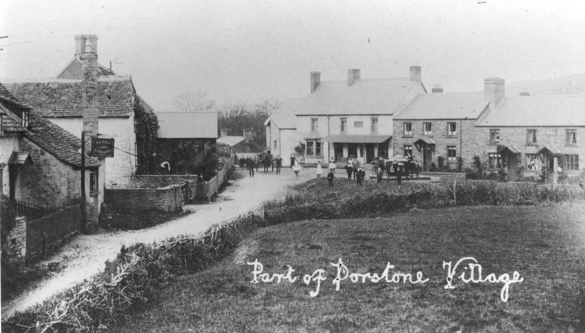 [DRAFT 2026-05-07] Edwardian monochrome postcard captioned 'Part of Dorstone Village' in cursive overlay, looking along the village street past a stone cottage with a hanging pub sign at left; a row of two-storey houses lines the right side of the road, with a small group of villagers and children standing on the green between them.